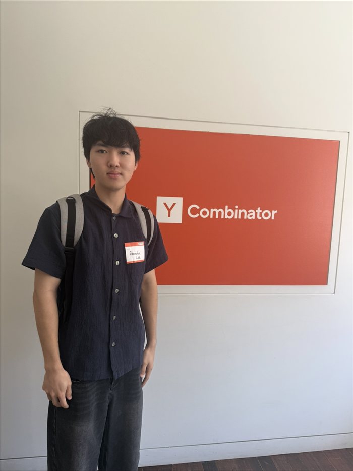 Brandon Lee standing in front of the Y Combinator sign wearing a name tag